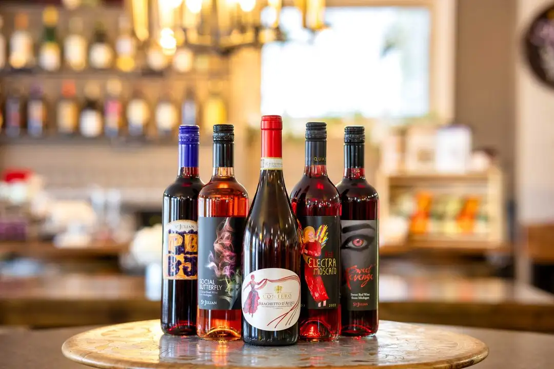 A row of sweet red and rosé wine bottles on a barrel-top table