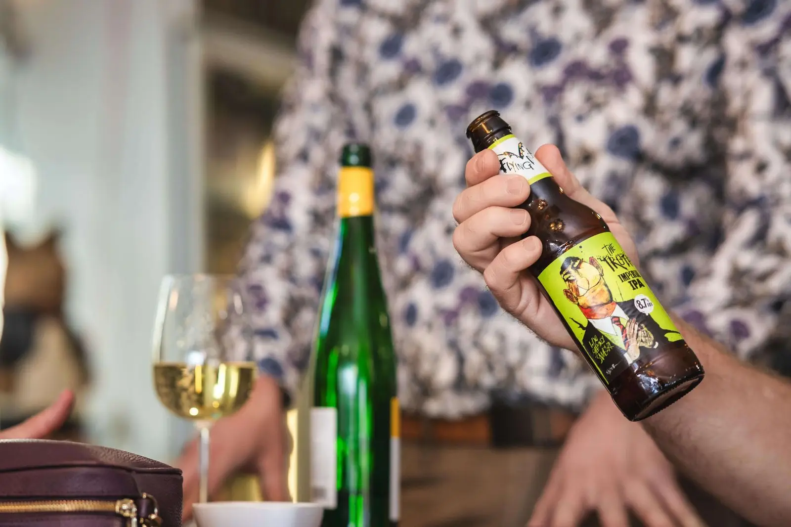 A guest holding a craft imperial IPA next to a glass of white wine